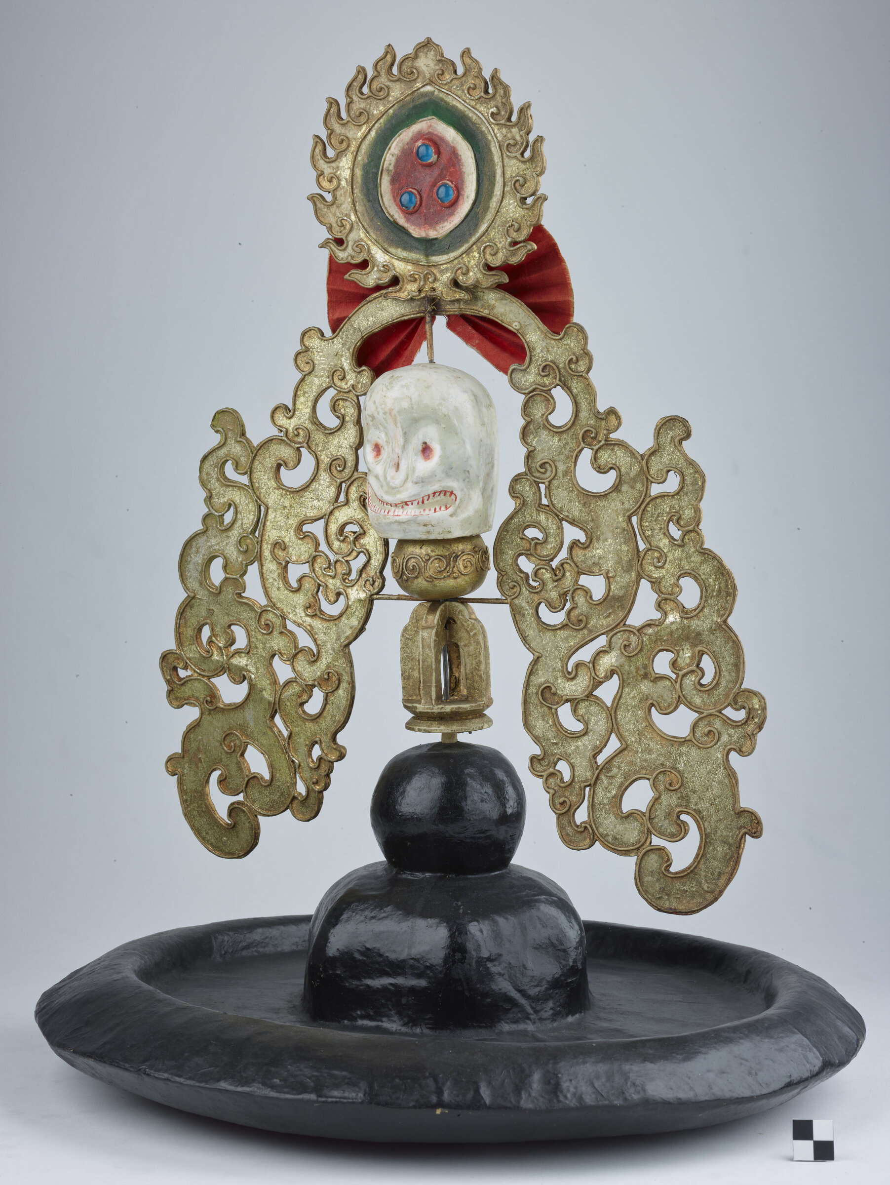 A ceremonial black hat crown with gold filigree side panels and a skull ornament, associated with the ZhaNag Black Hat dance.